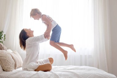 Anne, anaokulundaki çocuğuyla evde oynuyor, yatakta zıplıyor ve uçuyor.