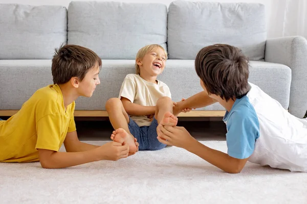 Happy positive children, tickling on the feet, having fun together, boy brothers at home having wonderful day of joy together