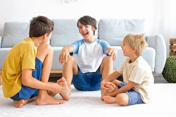 Happy positive children, tickling on the feet, having fun together, boy brothers at home having wonderful day of joy together