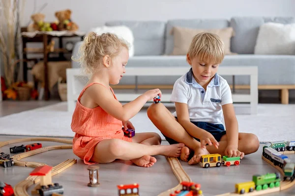 Two sweet children, siblings, playing with trains at home together