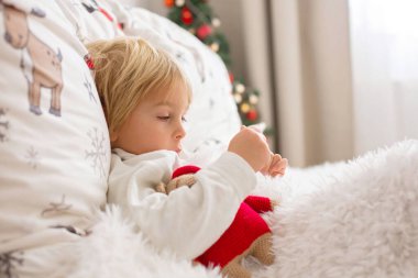 Güzel sarışın çocuk, ateşi olan hasta çocuk, Noel 'de yatakta yatıyor, öksürüyor ve burnu akıyor.