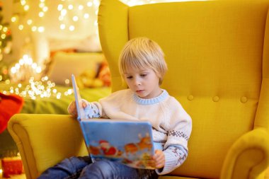 Tatlı çocuk, oğlum, Noel için süslü bir odada sarı bir koltukta oturuyor, rahat bir yer.