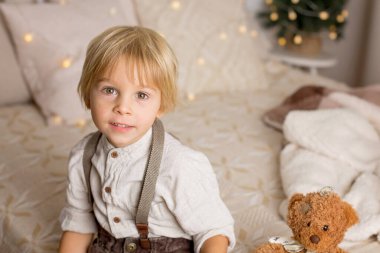 Çocuk yatakta oturuyor, boho stili, gülümsüyor, şık giyimli şirin bir çocuk.