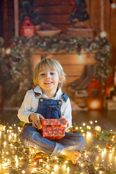 Toddler child, cute blond boy, sitting on the floor with pet dog, christmas lights around him