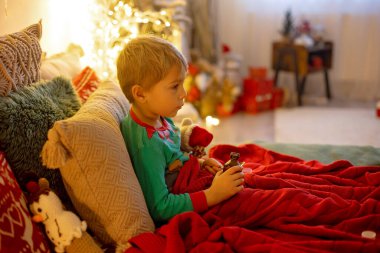 Küçük sarışın çocuk, yatağında hasta yatıyor, şurup içiyor, üzülüyor.