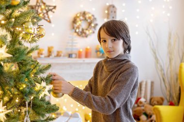 Tatlı çocuk, oğlum, Noel için dekore edilmiş odada oynuyor, Noel ağacını süslüyor.