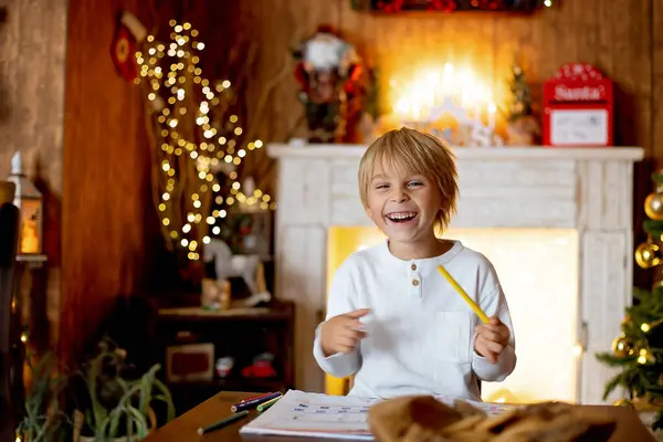 漂亮的金发碧眼的孩子 年轻的学生 在装饰过的房子里给圣诞老人写信 喝牛奶 吃饼干 填充物和针织玩具 — 图库照片