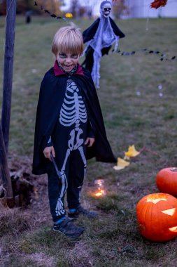 Parkta Cadılar Bayramı kostümlü iki çocuk mum ve dekorasyonla balkabağı oyup oynuyorlar.