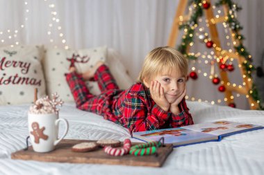 Güzel sarışın çocuk, genç okul çocuğu, süslü bir evde okul için ödev yazıyor, süt içiyor ve kurabiye yiyor. Işıklar ve örgü oyuncaklar
