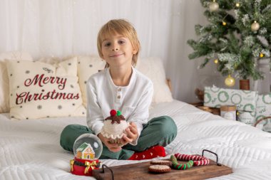 Güzel sarışın çocuk, genç okul çocuğu, süslü bir evde okul için ödev yazıyor, süt içiyor ve kurabiye yiyor. Işıklar ve örgü oyuncaklar