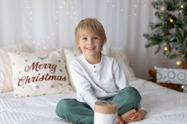 Güzel sarışın çocuk, genç okul çocuğu, süslü bir evde okul için ödev yazıyor, süt içiyor ve kurabiye yiyor. Işıklar ve örgü oyuncaklar