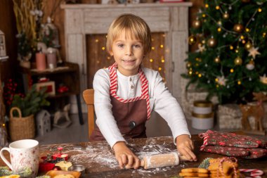 Güzel sarışın çocuk, genç okul çocuğu, süslü bir evde okul için ödev yazıyor, süt içiyor ve kurabiye yiyor. Işıklar ve örgü oyuncaklar