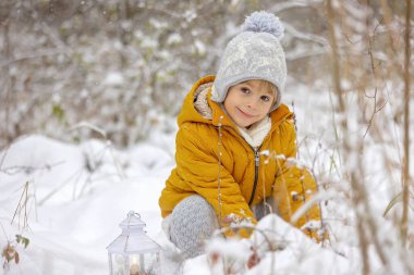 Şirin küçük sarışın çocuk, kış günü karda oynuyor, örgü bezler içinde.