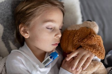 Hasta çocuk, küçük çocuk ateşler içinde yatağında yatıyor, evde dinleniyor.
