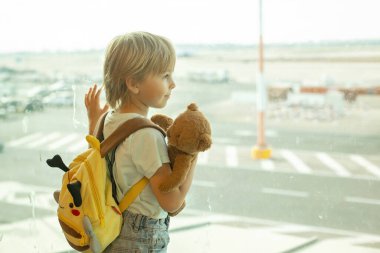Çocuk, havaalanının penceresinden uçaklar havalanıyor ve iniyor. Tatil için uçağa binmeyi bekliyor.