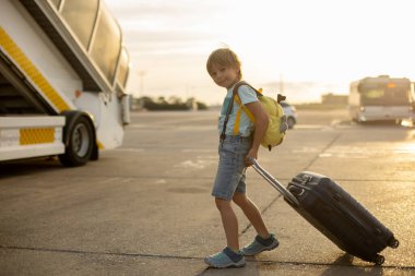 Sevimli sarışın çocuk, sırt çantalı çocuk, gün batımında havaalanında uçağa binmiş, dışarıdan manzaranın tadını çıkarıyor.