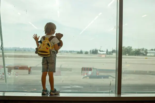 Child, watching from the window of the airport the planes, taking off and landing while waiting at  to board the aircraft for a holiday