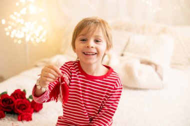 Beyaz ve kırmızı bileziklerle oynayan sevimli anaokulu çocuğu. Martenitsa, beyaz ve kırmızı iplik türleri, Bulgar folklor geleneği, Mart ayında baharı karşılama, süs sembolü, iyi bir sağlık dileği