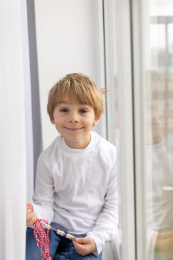 Tatlı çocuk, sarışın çocuk, beyaz ve kırmızı bileklikle oynuyor, martenitsa.