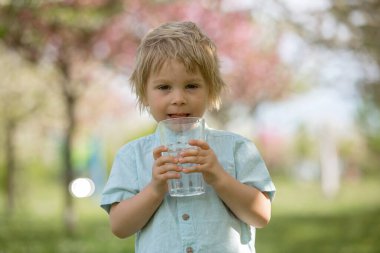 Güzel sarışın çocuk, evlat, sıcak bir yaz gününde parkta su içiyor.