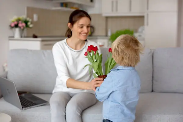 Child, toddler boym holding flowers for mother for her holiday, mothers day, red tulips in a beautiful vase