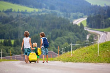 Küçük çocuklar, sırt çantaları ve sutcase ile erkek kardeşler, doğal dağlara yolda seyahat