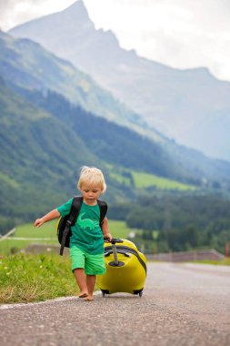 Küçük çocuklar, sırt çantaları ve sutcase ile erkek kardeşler, doğal dağlara yolda seyahat