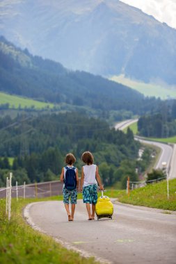 Küçük çocuklar, sırt çantaları ve sutcase ile erkek kardeşler, doğal dağlara yolda seyahat