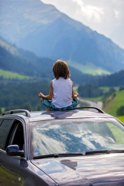 Sevimli çocuk, bir araba tavanda oturan çocuk, doğanın sessizliğinin tadını meditasyon, doğal dağlara giden yolda seyahat, yaz