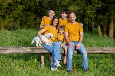 Parkta çocuklu ve evcil köpekli mutlu bir aile, gün batımında birlikte eğleniyorlar.