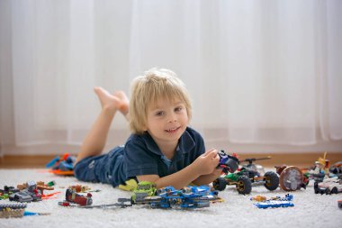 Tatlı çocuk, sarışın çocuk, Colofrul plastik bloklarla oynuyor, inşaat oyuncakları, araba ve uçak yapıyor.