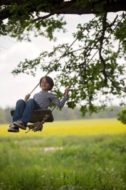 Tatlı çocuk, preteen çocuk, yağlı tohum alan yakın bir ağaçta bir ahşap salıncak üzerinde sallanan