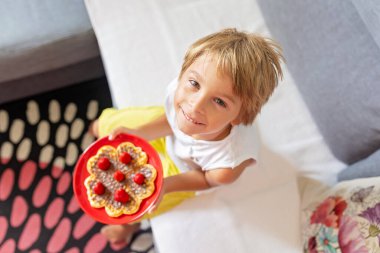 Tatlı bebek doğum günü çocuğu, evde çilekli Belçika waffle 'ı ve çikolata yiyor.