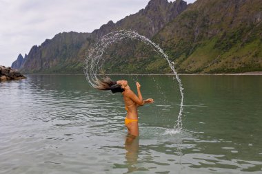 Senja adasındaki Ersfjord Sahili 'nin tadını çıkaran kadın Norveç, Norveç' teki dağların üzerindeki manzara manzarası.