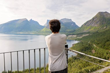 Children, standing on the edge of a 44 meter long viewing platform, overlooking the water of Bergsfjord, enjoying the view on Senja island, Northern Norway clipart