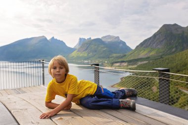 Çocuklar, 44 metre uzunluğundaki izleme platformunun kenarında durarak, Bergsfjord 'un suyuna bakarak, Kuzey Norveç' teki Senja adasının manzarasının tadını çıkarıyorlar.