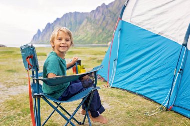 Kuzey Norveç, Senja 'daki Ersfjord plajında kamp yaparken sahilde yemek yiyen mutlu çocuklar. Çocuklar dışarıda öğle yemeği yiyor.