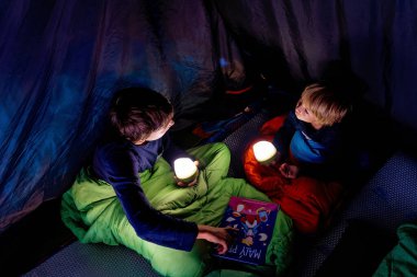 Çocuklar, çocuklar kardeşler, kampta bir çadırda eğleniyorlar, gülüyorlar ve kitap okuyorlar.