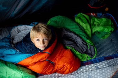 Çocuklar, çocuklar kardeşler, kampta bir çadırda eğleniyorlar, gülüyorlar ve kitap okuyorlar.