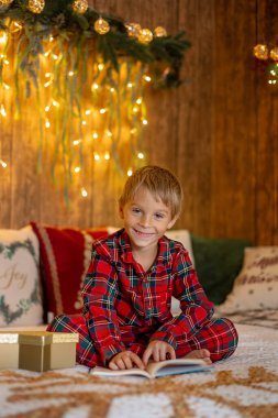 Tatlı sarışın çocuk, çocuk, Noel 'i evde kutluyor, tatiller için dekore edilmiş oda, çocuk kitapları okuyor ve oyun oynuyor.