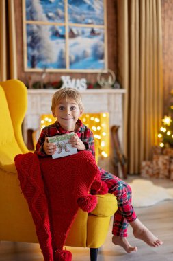 Tatlı sarışın çocuk, çocuk, Noel 'i evde kutluyor, tatiller için dekore edilmiş oda, çocuk kitapları okuyor ve oyun oynuyor.