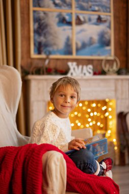 Tatlı sarışın çocuk, çocuk, Noel 'i evde kutluyor, tatiller için dekore edilmiş oda, çocuk kitapları okuyor ve oyun oynuyor.
