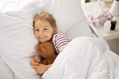 Oyuncak ayıyla tatlı sarışın anaokulu çocuğu, hasta yatıyor, güneşli yatak odasında.