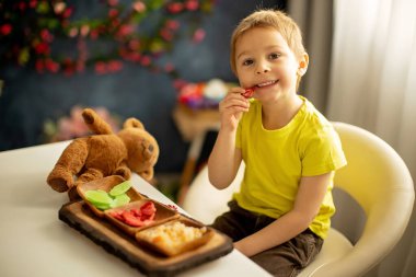 Sevimli küçük anaokulu çocuğu, çocuk, evde kurutulmuş meyve yiyor, çilek, kavun, ananas tabakta