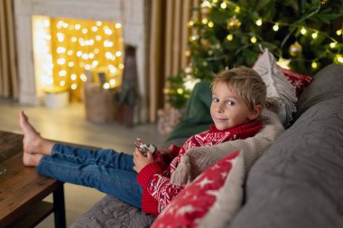 Tatlı sarışın çocuk, çocuk, Noel 'i evde kutluyor, tatiller için dekore edilmiş oda, çocuk kitapları okuyor ve oyun oynuyor.