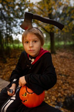 Cadılar Bayramı kostümlü bir ormanda çocuk, mumlarla ve dekorasyonla oyulmuş balkabakları, ürkütücü konsept, Cadılar Bayramı teması