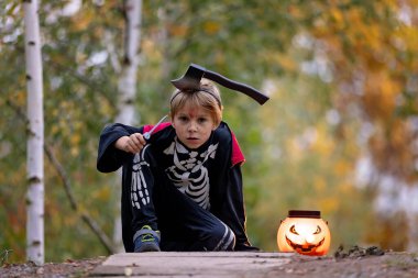Cadılar Bayramı kostümlü bir ormanda çocuk, mumlarla ve dekorasyonla oyulmuş balkabakları, ürkütücü konsept, Cadılar Bayramı teması