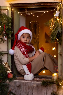 Güzel sarışın çocuk, çocuk, Noel 'de sütle süslenmiş bir pencerede oturuyor, süt içiyor ve elma yiyor, Noel Baba' yı bekliyor, Noel Baba 'yı, kışın