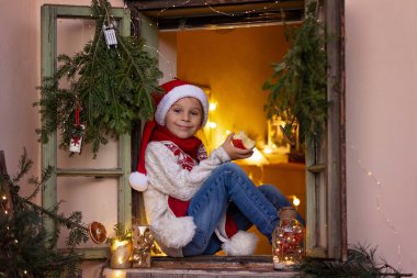 Güzel sarışın çocuk, çocuk, Noel 'de sütle süslenmiş bir pencerede oturuyor, süt içiyor ve elma yiyor, Noel Baba' yı bekliyor, Noel Baba 'yı, kışın