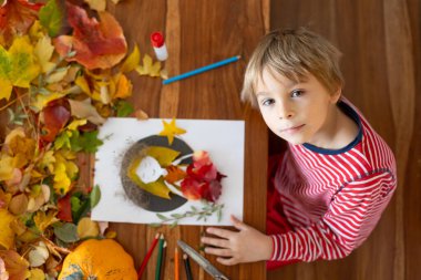 Tatlı çocuk, evlat, evde sonbaharda sanat ve zanaat yaparken yaprakları yapıştırmak...